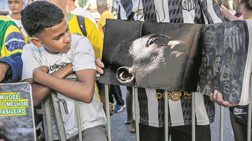 Küçük bir çocuk 29 Aralık günü yaşamını yitiren Pelé'ye saygılarını sunmak için Brezilya'nın Santos kentindeki stadyumun dışında sırada beklerken bir başka taraftarın elindeki kitaba bakıyor. (Dado Galdieri/New York Times)