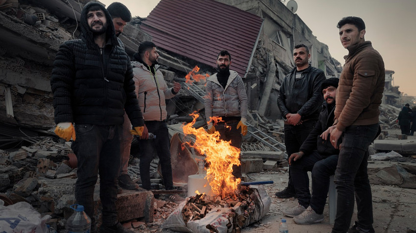 Antakya'nın eski mahallesinde yakılan ateşin başında ısınmaya çalışan erkekler. (Emily Garthwaite/The New York Times)