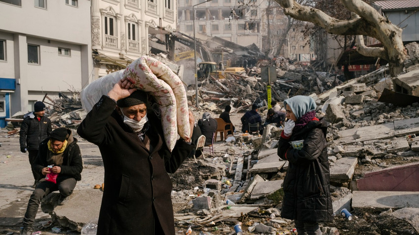 Kahramanmaraş'taki depremde çöken bir binanın yanında oturanlar, 10 Şubat. Büyük depremden sağ kurtulan kişiler arasında hükümetin krizi yönetme biçimi konusundaki korku artıyor (Emin Özmen/The New York Times)