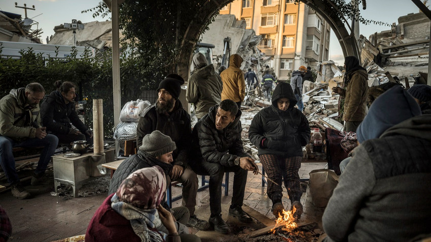 Antakya'da çöken bir binanın yanında yatıkları ateşle ısınmaya çalışan bir aile. 8 Şubat 2023. (Sergey Ponomarev/New York Times)