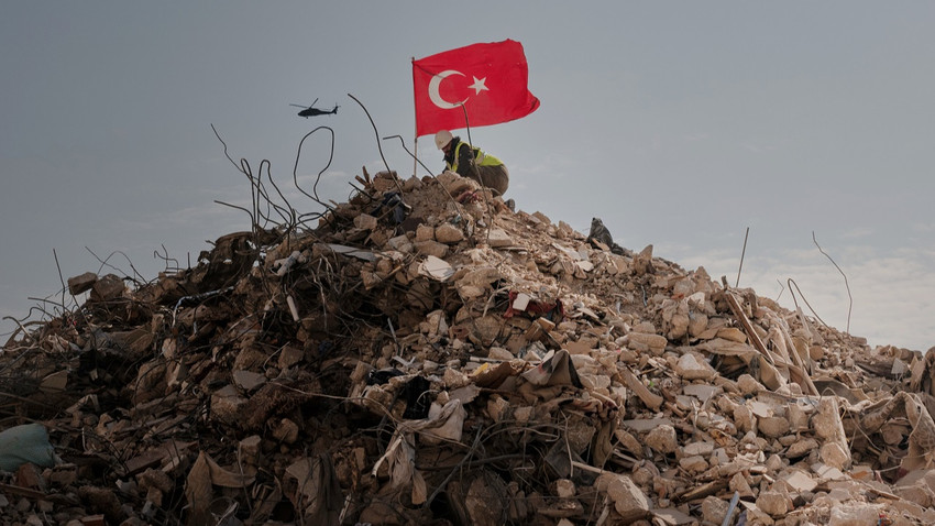 Bir kurtarma görevlisi Antakya'da enkaza dönen sekiz katlı bir binanın tepesine Türk bayrağı dikiyor, 11 Şubat 2023 (Fotoğraf: Emily Garthwaite/The New York Times)