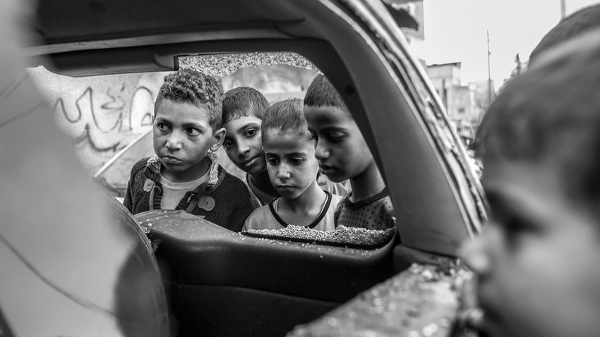 Han Yunus'ta BM tarafından işletilen bi rokulun önünde İsrail hava saldırısında hasar gören bir arabanın etrafında toplanan çocuklar, 19 Ekim (Fotoğraf: Samar Abu Elouf/The New York Times)