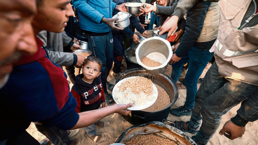 Yerlerinden edilmiş Gazzeliler Ramazan’ın ilk gününde bölgenin güneyindeki Refah’ta bir yardım kuruluşu tarafından dağıtılan iftar yemeğinden almaya çalışıyor. (GETTY IMAGES)